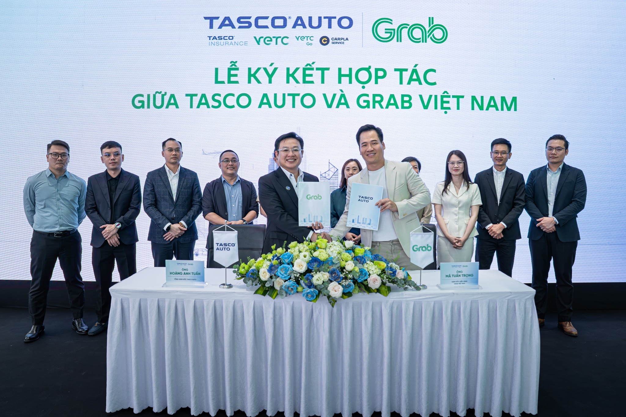 Hình ảnh sự kiện lễ ký kết hợp tác giữa Tasco Auto và Grab Việt Nam. Đại diện hai bên, ông Hoàng Anh Tuấn (Tasco Auto) và ông Mã Tuấn Trọng (Grab Việt Nam), trao đổi văn bản thỏa thuận cùng các đại biểu tham dự.